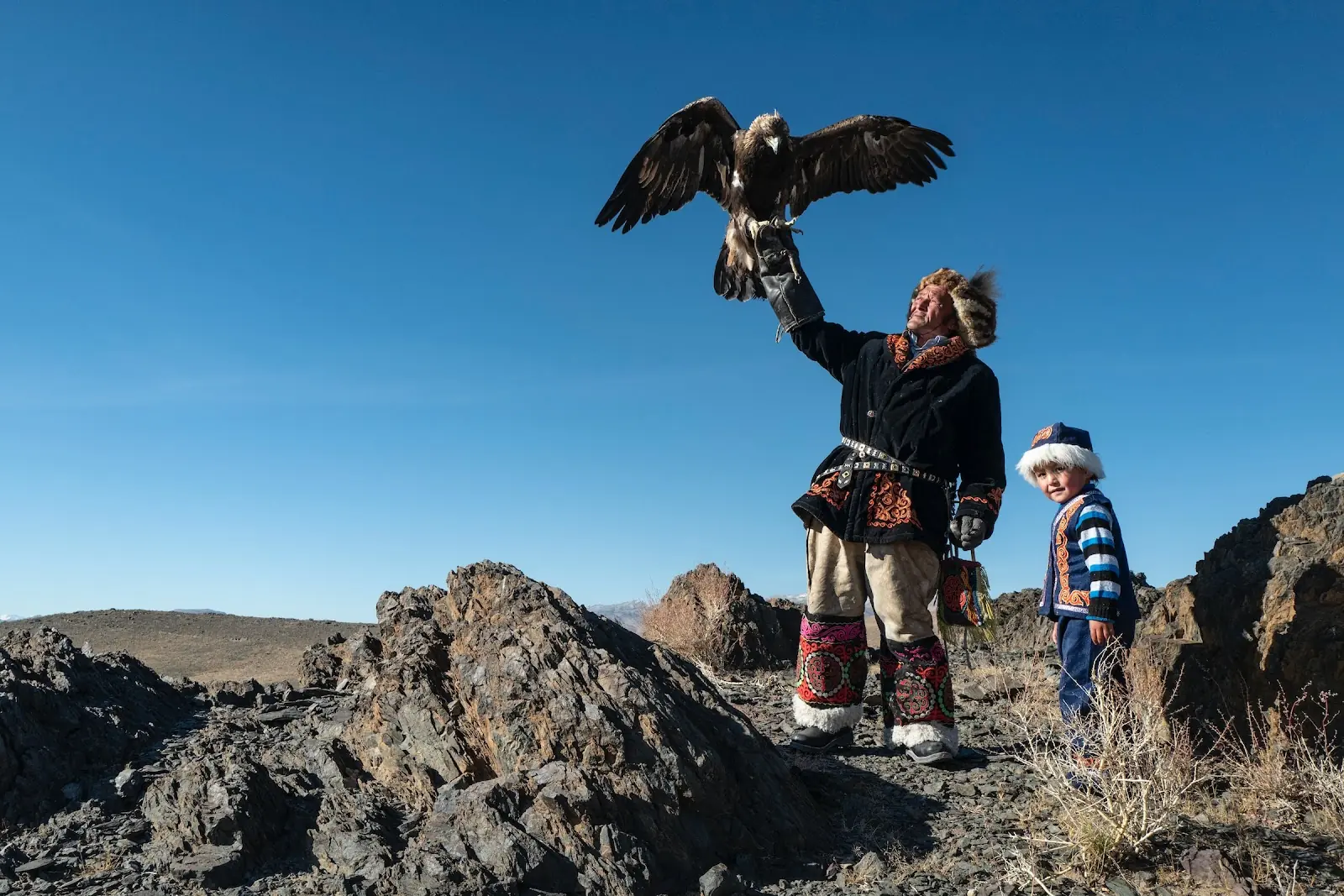 A Mongolian man flies a bird of prey with a child.