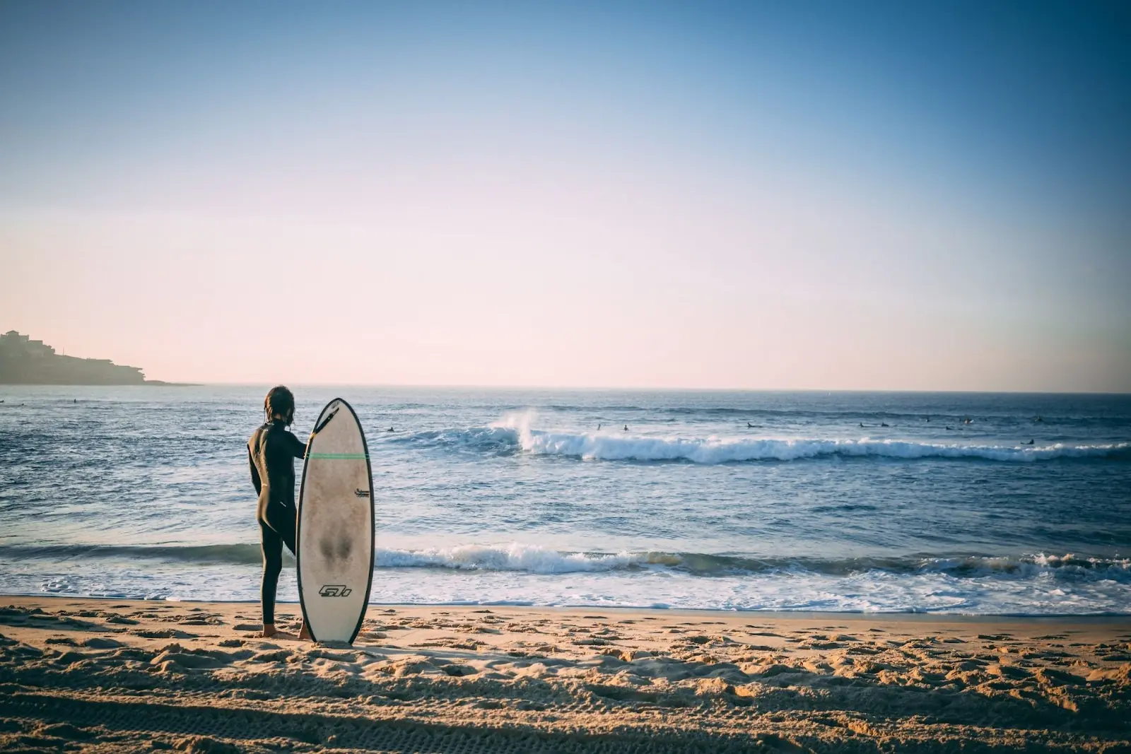 Surfer stood holding his surfboard on Australian beach looking out over the sea.