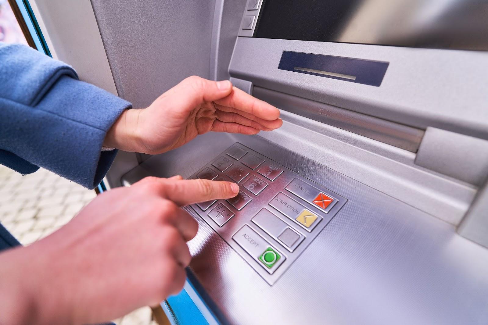Person dials and hides with other hand for security purposes a PIN code on the keyboard of atm bank to withdraw travel cash