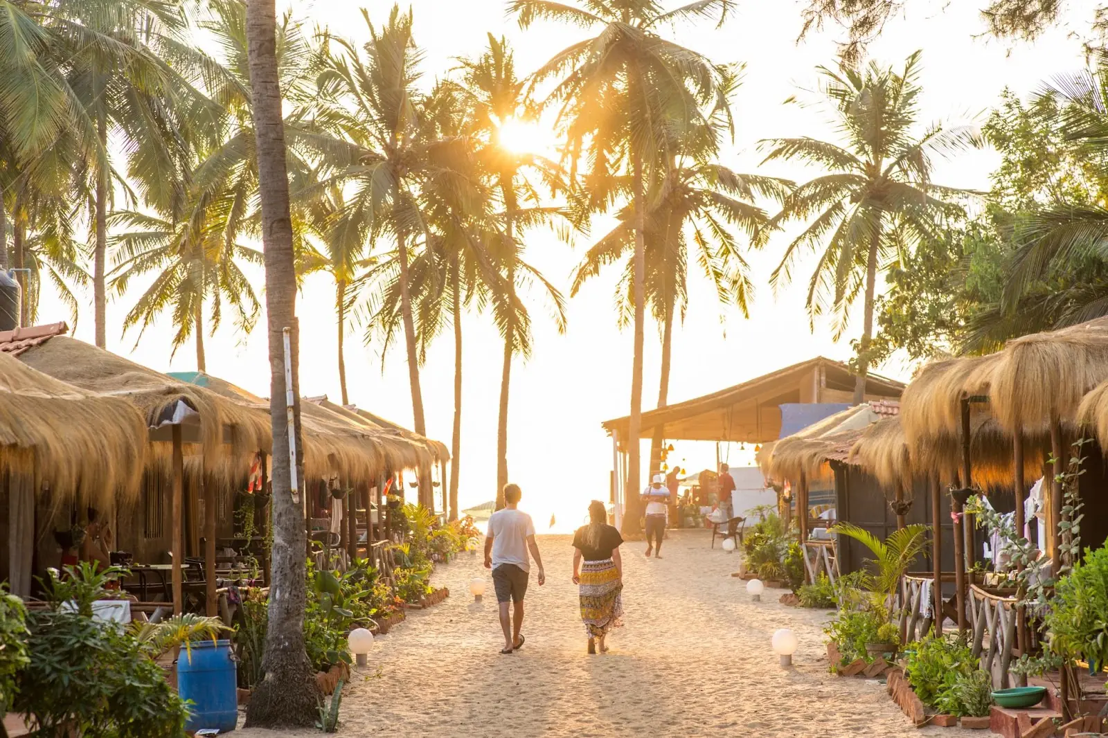  tourist couple walking past some huts towards the sunset over the sea in Goa. - Valentines