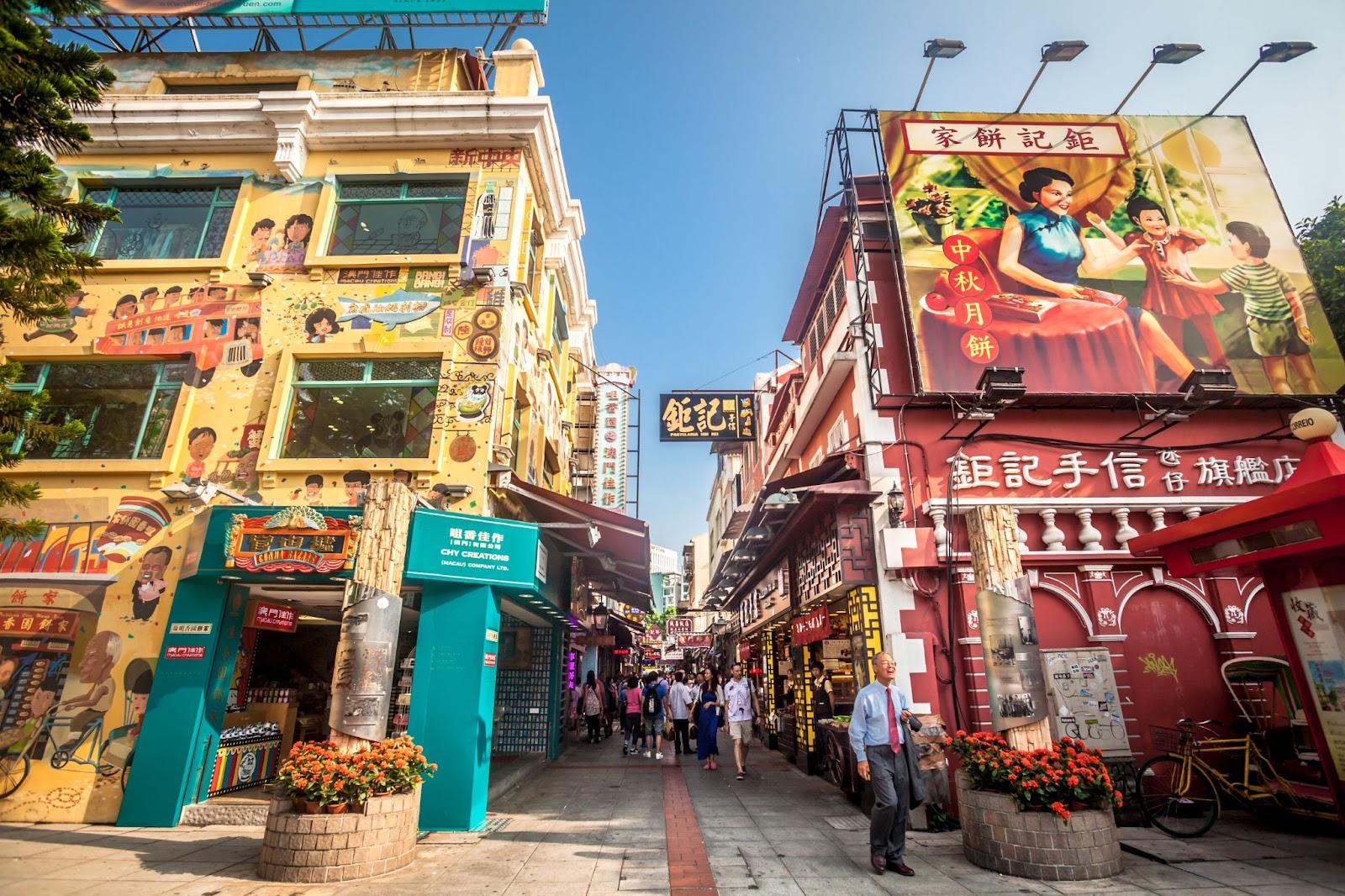 Macau, Macau S.A.R. - September 19, 2015: Tourists and shoppers walking along a narrow street with colourful building in central Macau with many shops and restaurants.