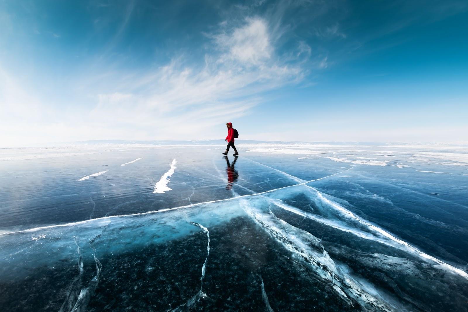 Man tourist walking on the ice of Baikal lake. Winter landscape of Baikal lake, Siberia, Russia.