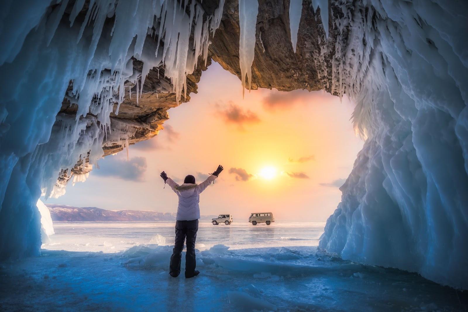Traveller woman raise up hand freedom and enjoy view of beautiful landscape natural breaking ice in frozen cave at Lake Baikal, Siberia, Russia.