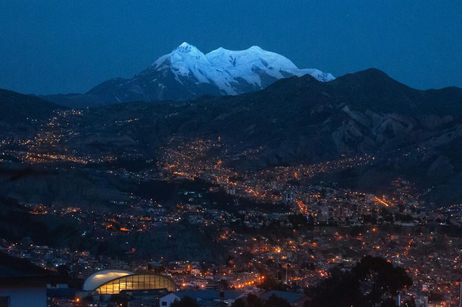 Mount Illimani, the guardian of La Paz, Bolivia. Its peaks barely illuminated by the last rays of daylight. The city already lit up.