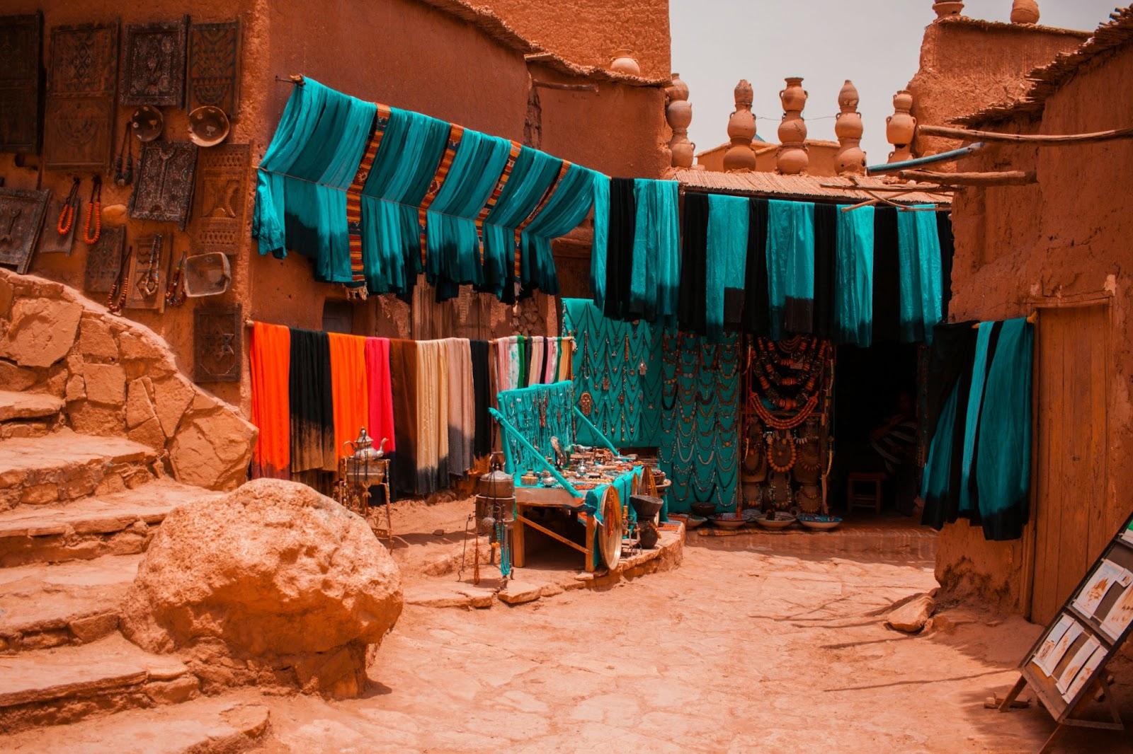 View assorted-coloured textiles hanging outside building in Aït Benhaddou. To buy with Moroccan dirhams (MAD)