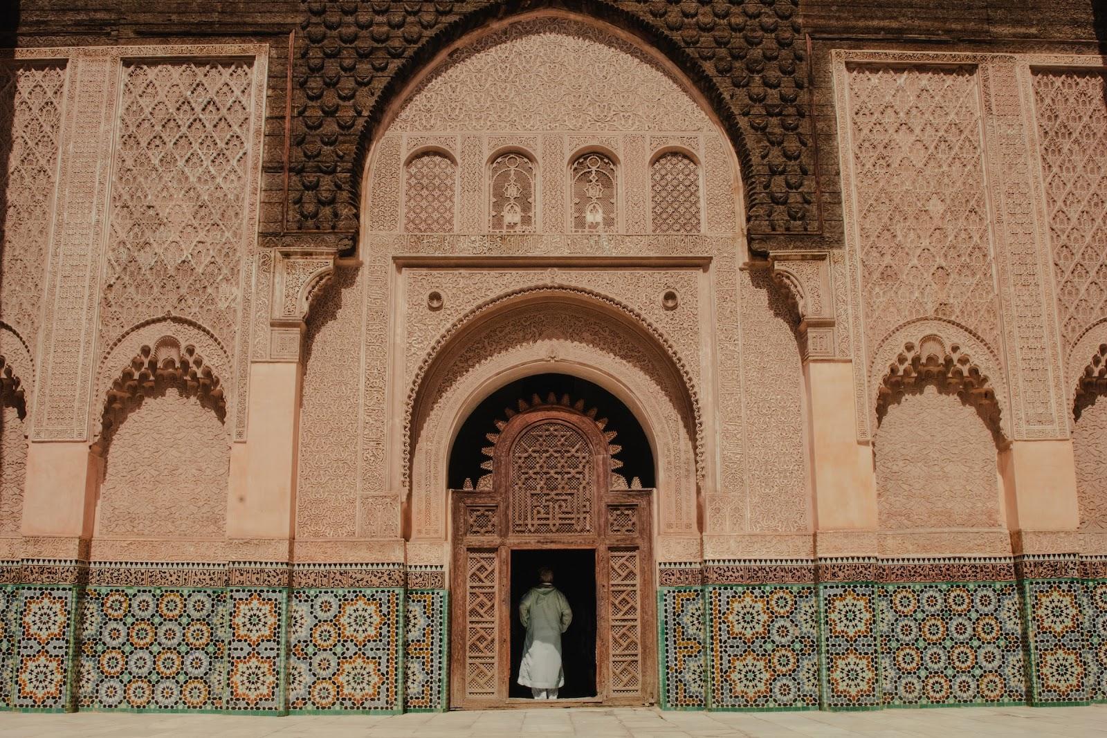 An ornate sandstone temple covered with green and yellow symmetrical tiles. Pay entrance fees in MAD