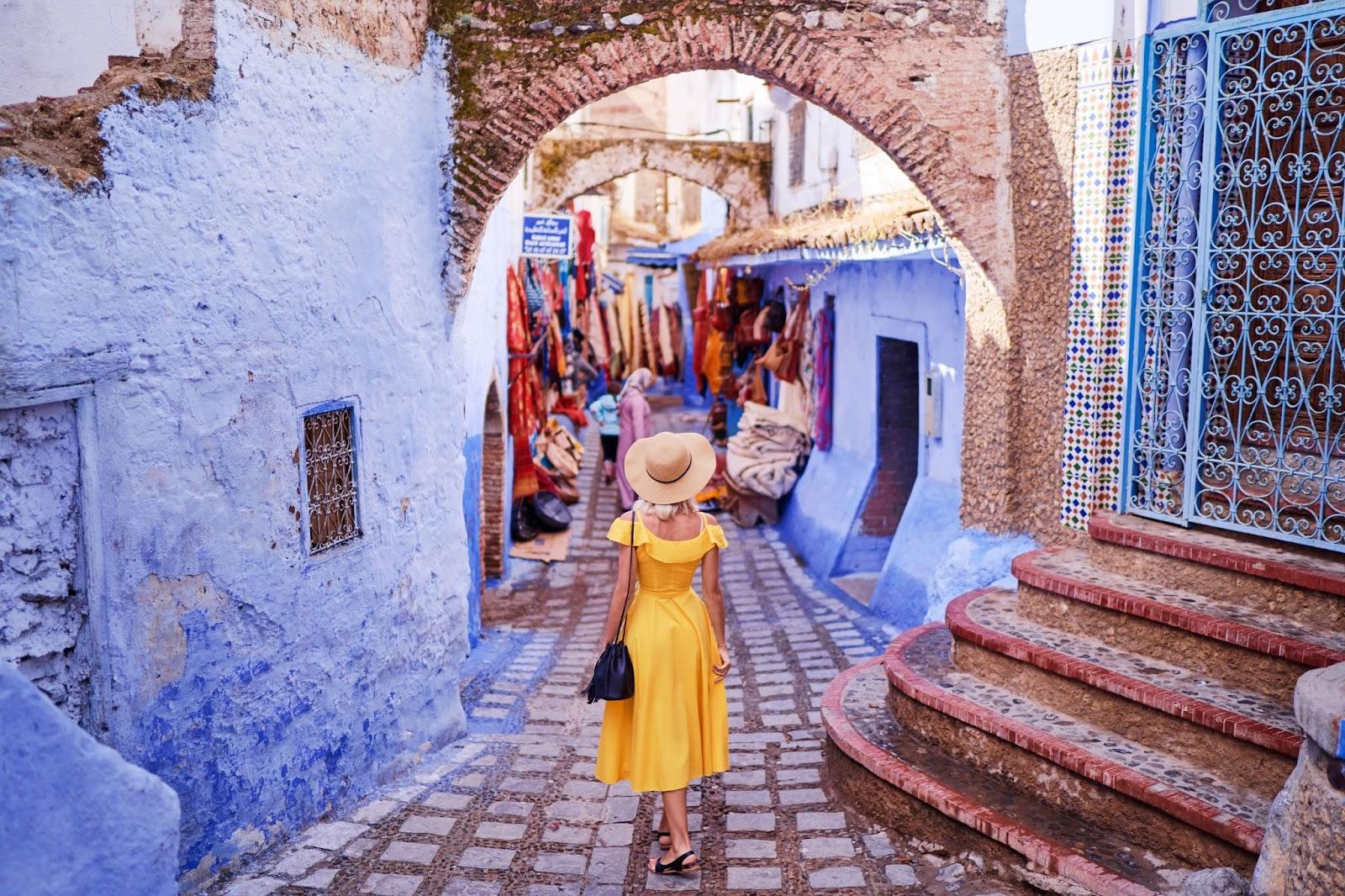 Colorful traveling by Morocco. Young woman in yellow dress walking in medina of blue city Chefchaouen.