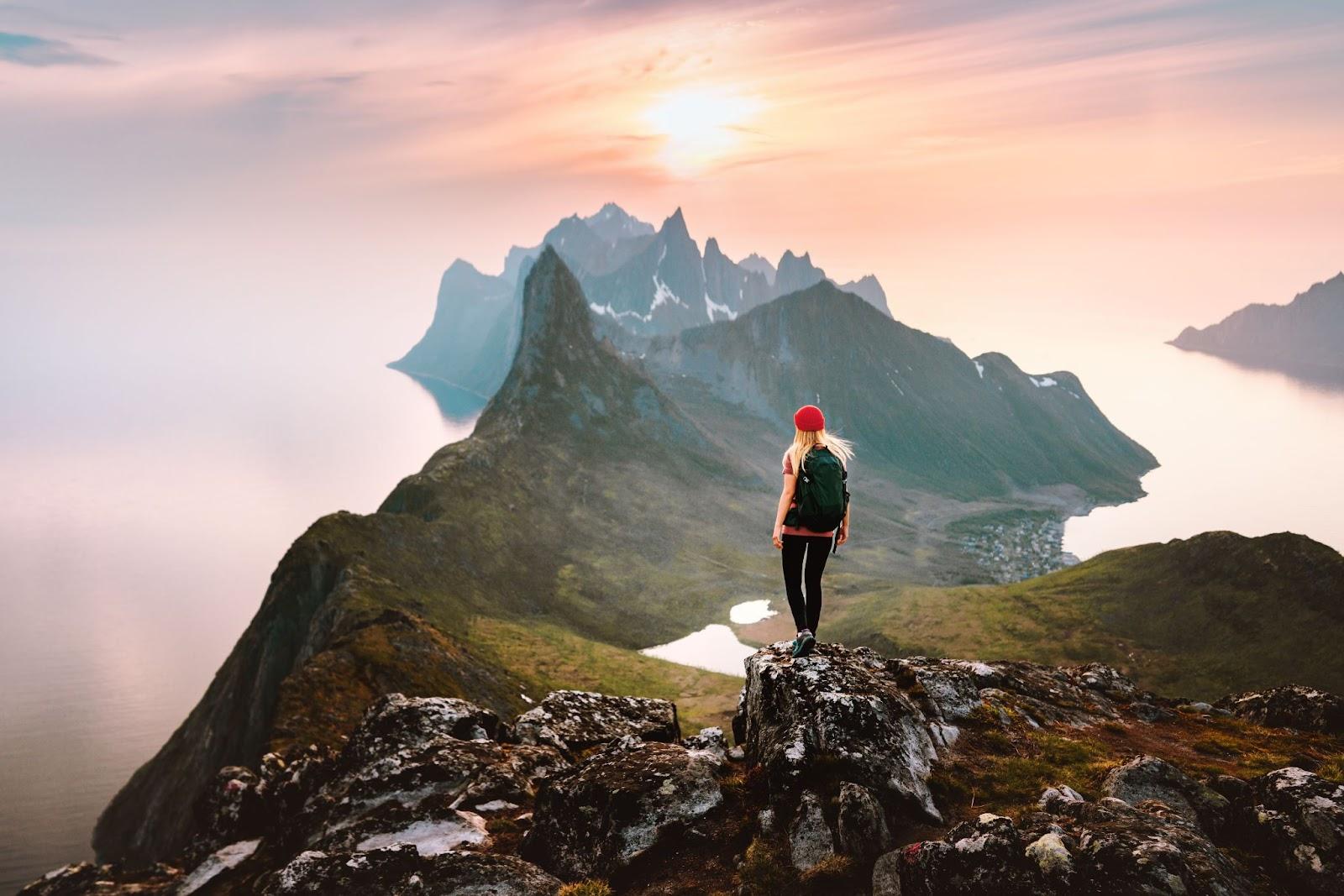 Traveller woman hiking solo in mountains of Norway outdoor activity travel summer vacations healthy lifestyle girl tourist enjoying sunset view on summit exploring Senja island