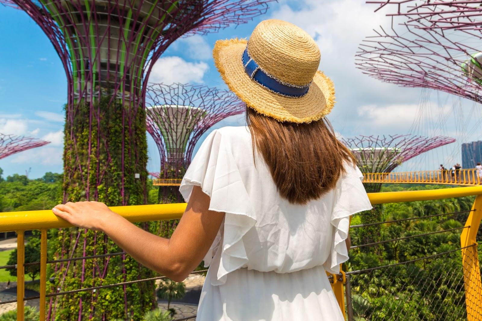 Woman traveller wearing white dress and straw hat at Skyway bridge at Gardens by the Bay in Singapore