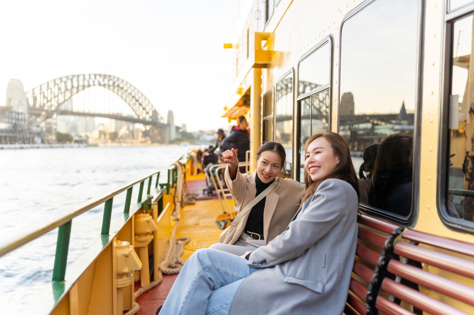 Happy Asian woman friends travel in the city sitting on ferry boat crossing Sydney harbour in Australia. Attractive girl enjoy and fun urban outdoor lifestyle shopping and travel on holiday vacation.