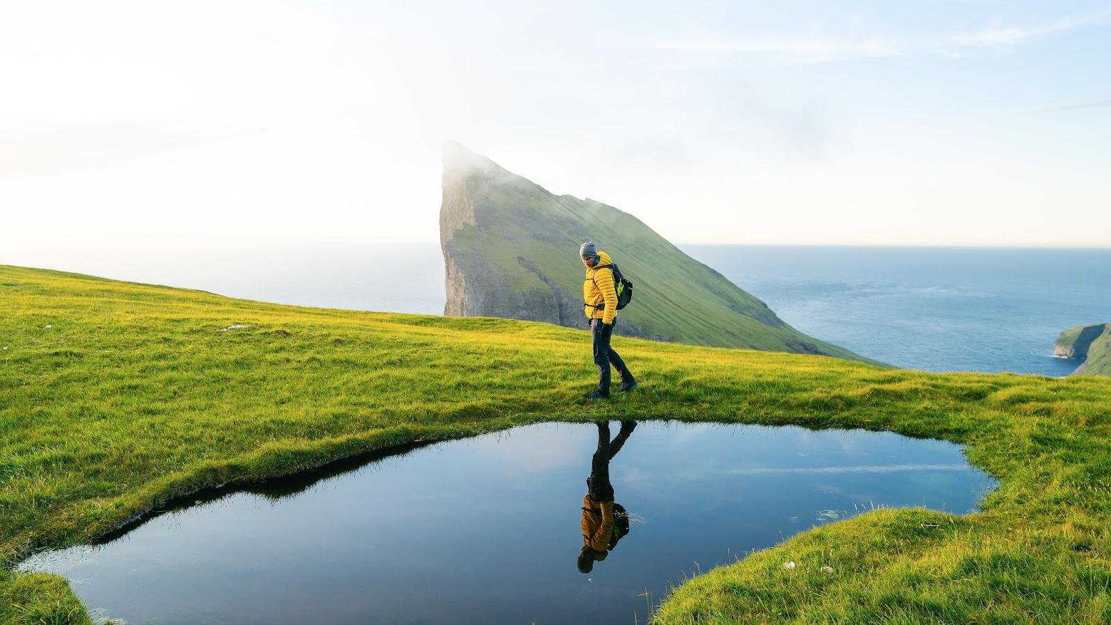 Lonely tourist in yellow jacket looking over majestic fjords. Faroe Islands. Landscape photography