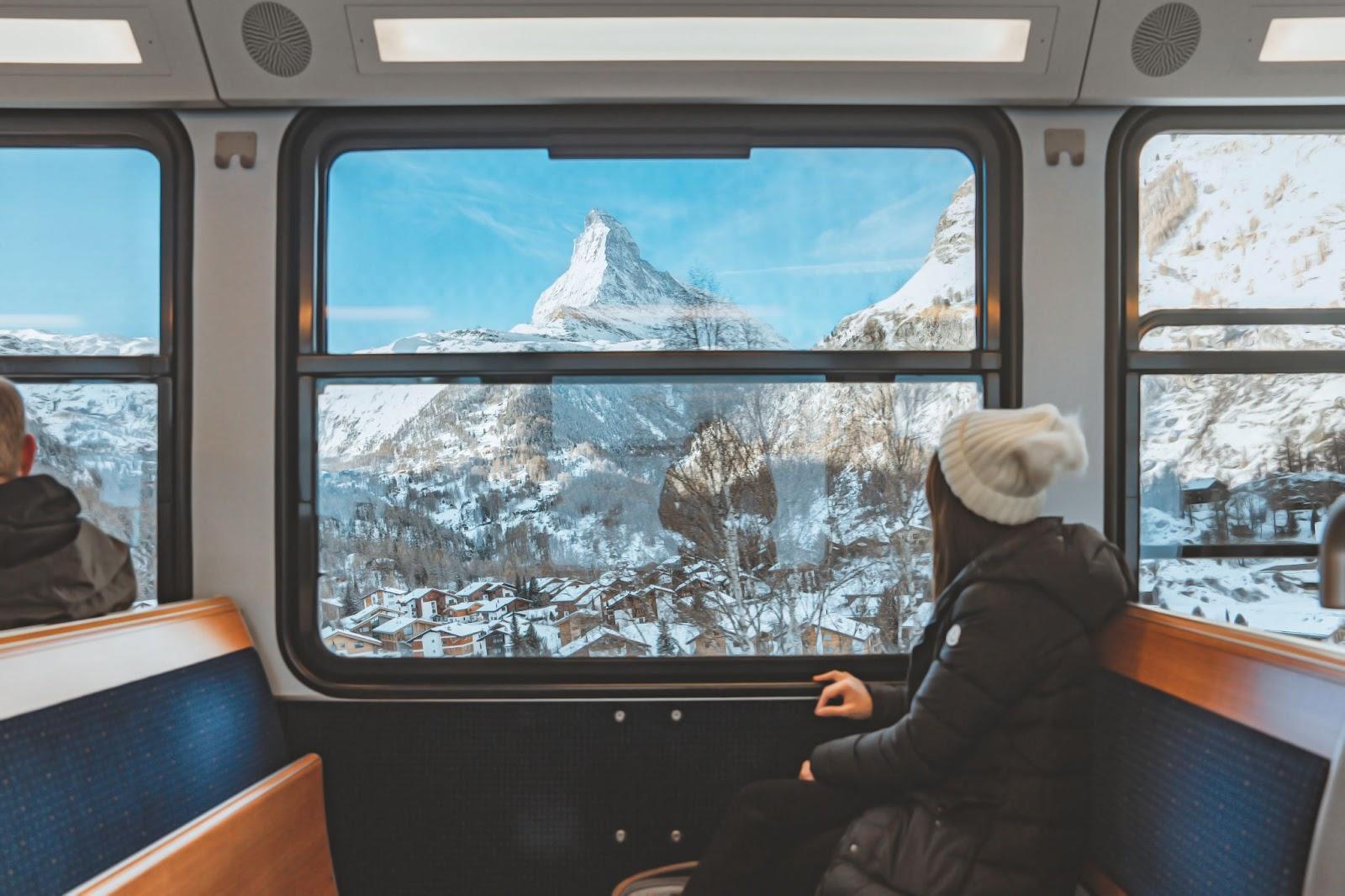 Blur foreground - young woman traveling looking out the window enjoying in Swiss Alps with the Matterhorn in winter background while sitting in the train. Tourist travel concept.