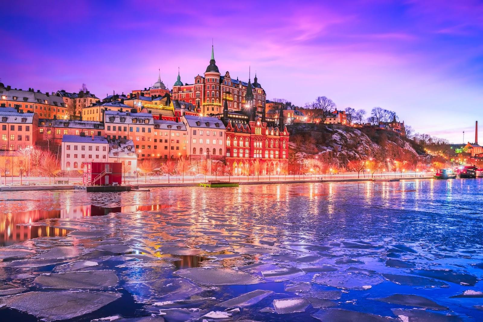 Stockholm, Sweden. Mariaberget and Sodermalm island in winter. Beautiful orange, violet and pink sky at twilight, reflected in frozen water of lake Malaren.