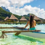 Outrigger Canoe - woman paddling in traditional French Polynesian Outrigger Canoe for recreational activity and watersport competition. Bora Bora with overwater bungalow resort hotel sport lifestyle