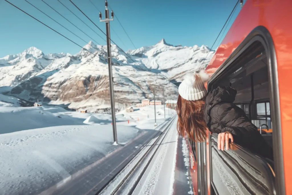 Happy woman traveler looks out from window traveling by train in beautiful winter mountains, Travel concept.