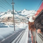 Happy woman traveler looks out from window traveling by train in beautiful winter mountains, Travel concept.